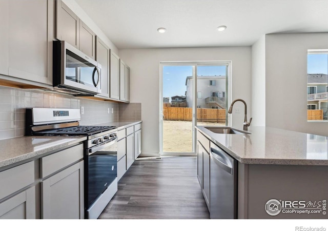 kitchen with stainless steel appliances, dark hardwood / wood-style flooring, light stone countertops, sink, and a kitchen island with sink