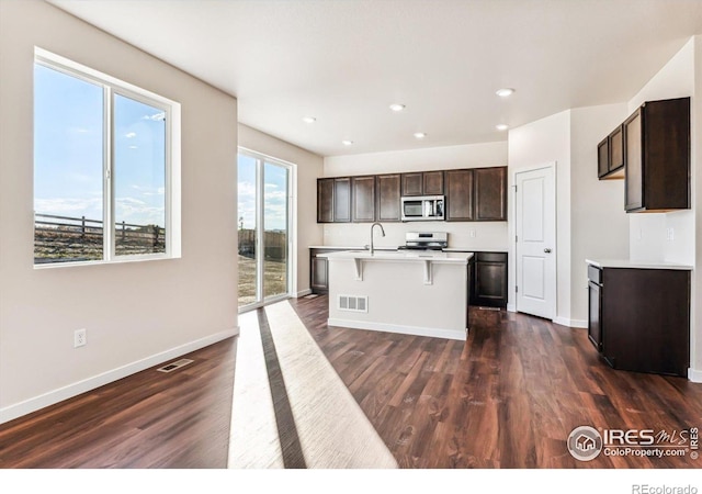 kitchen featuring a center island with sink, stainless steel appliances, dark brown cabinets, dark hardwood / wood-style floors, and sink