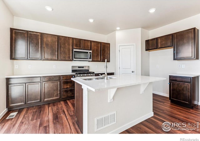 kitchen with stainless steel appliances, dark wood-type flooring, sink, and an island with sink