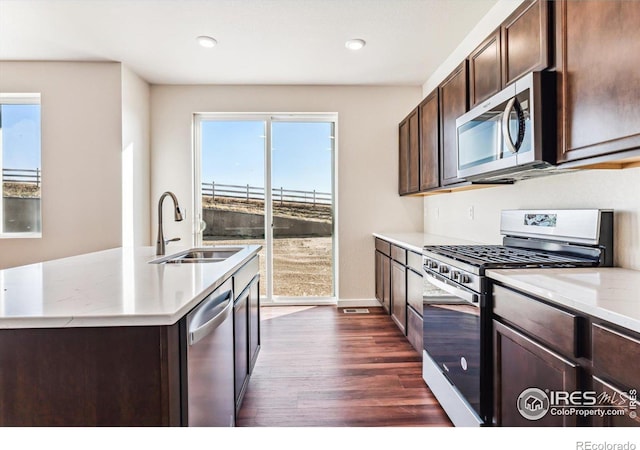 kitchen with sink, an island with sink, dark hardwood / wood-style floors, dark brown cabinets, and appliances with stainless steel finishes