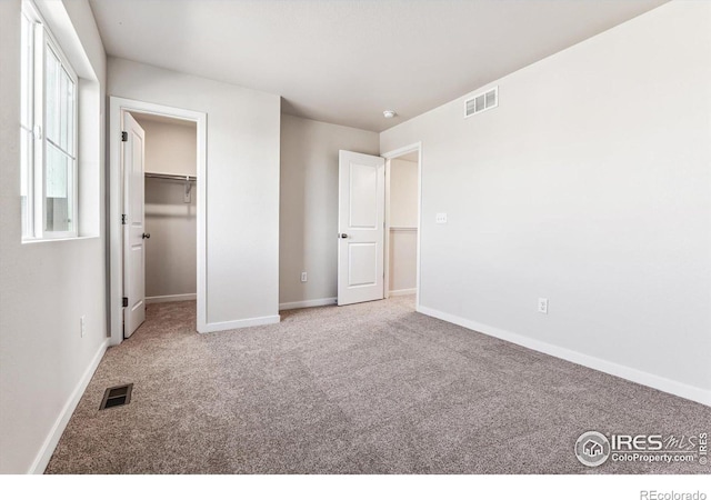 unfurnished bedroom with a closet, a walk in closet, and carpet flooring