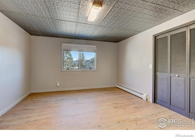 unfurnished bedroom with a closet, a baseboard radiator, and light wood-type flooring