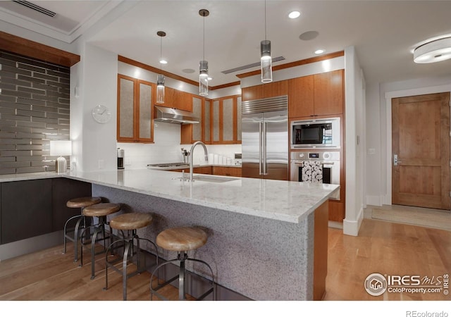 kitchen featuring sink, built in appliances, a kitchen bar, tasteful backsplash, and kitchen peninsula