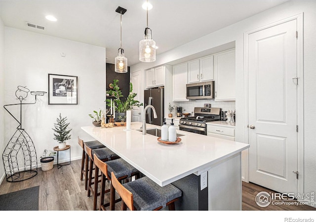 kitchen featuring white cabinetry, hardwood / wood-style flooring, pendant lighting, a breakfast bar, and appliances with stainless steel finishes