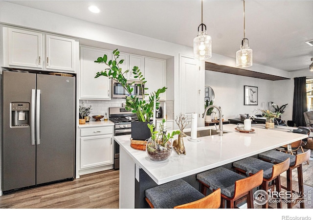 kitchen featuring sink, stainless steel appliances, light hardwood / wood-style floors, decorative light fixtures, and white cabinets