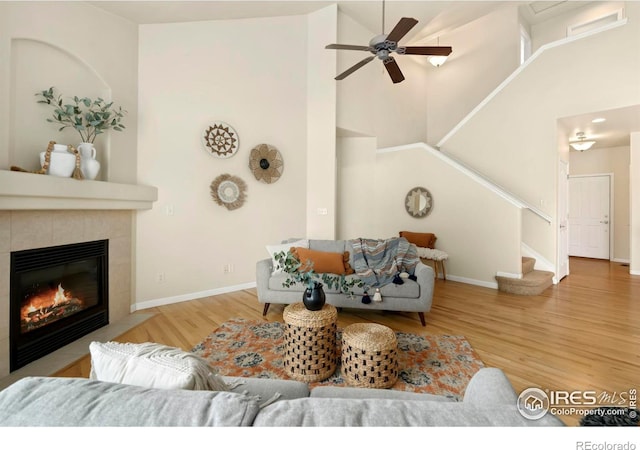 living room featuring hardwood / wood-style flooring, ceiling fan, high vaulted ceiling, and a tiled fireplace