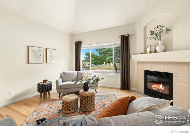 living room with a tile fireplace, light hardwood / wood-style flooring, and lofted ceiling