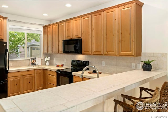 kitchen featuring black appliances, tile counters, a kitchen bar, and tasteful backsplash