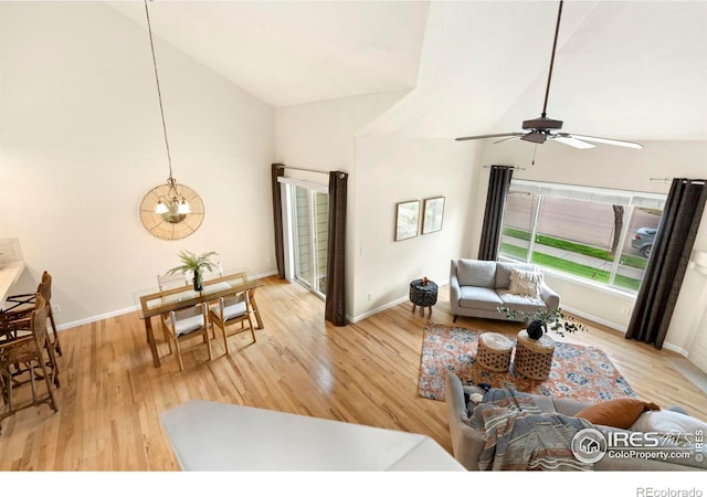 living room with ceiling fan with notable chandelier, light hardwood / wood-style floors, and high vaulted ceiling