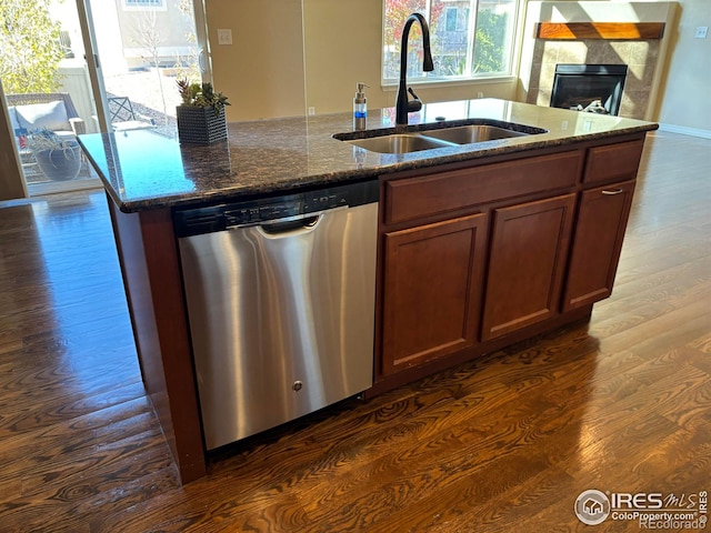 kitchen with dark hardwood / wood-style flooring, stainless steel dishwasher, dark stone counters, sink, and a center island with sink