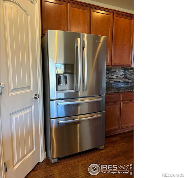 kitchen with stainless steel fridge, tasteful backsplash, dark wood-type flooring, and dark stone countertops