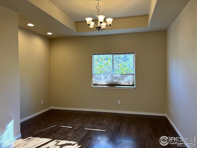 spare room with a raised ceiling, dark hardwood / wood-style floors, and an inviting chandelier