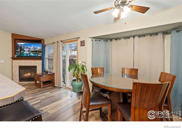 dining area featuring ceiling fan, wood-type flooring, a fireplace, and vaulted ceiling