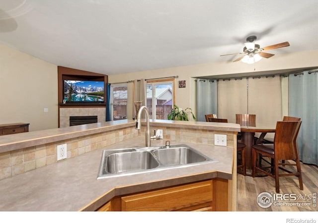 kitchen featuring ceiling fan, sink, a tile fireplace, light hardwood / wood-style floors, and lofted ceiling