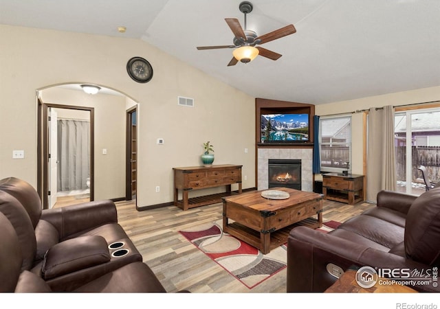 living room with ceiling fan, light hardwood / wood-style floors, a tile fireplace, and vaulted ceiling