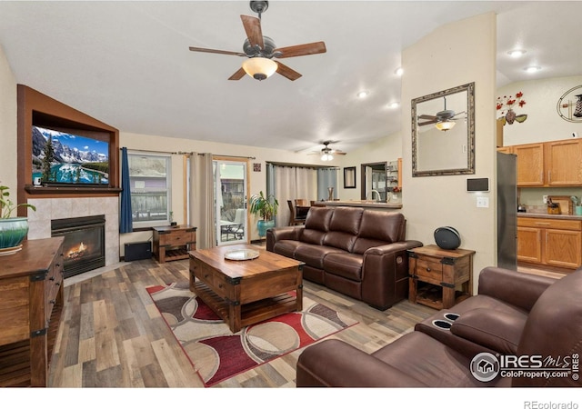 living room with a tiled fireplace, ceiling fan, light hardwood / wood-style flooring, and lofted ceiling