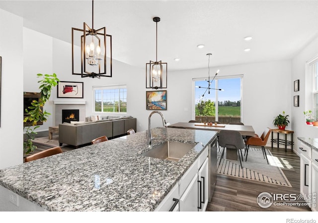 kitchen featuring light stone counters, stainless steel dishwasher, pendant lighting, white cabinets, and sink