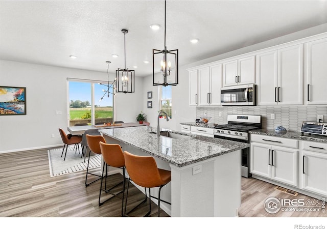 kitchen featuring stainless steel appliances, an island with sink, pendant lighting, sink, and white cabinetry