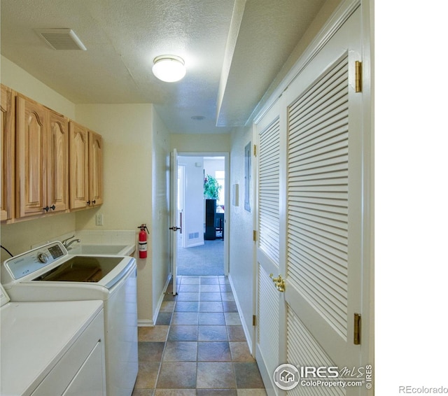 clothes washing area featuring sink, cabinets, washing machine and dryer, tile patterned floors, and a textured ceiling