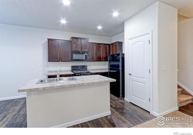 kitchen featuring dark brown cabinetry, dark wood-type flooring, sink, black appliances, and a center island with sink