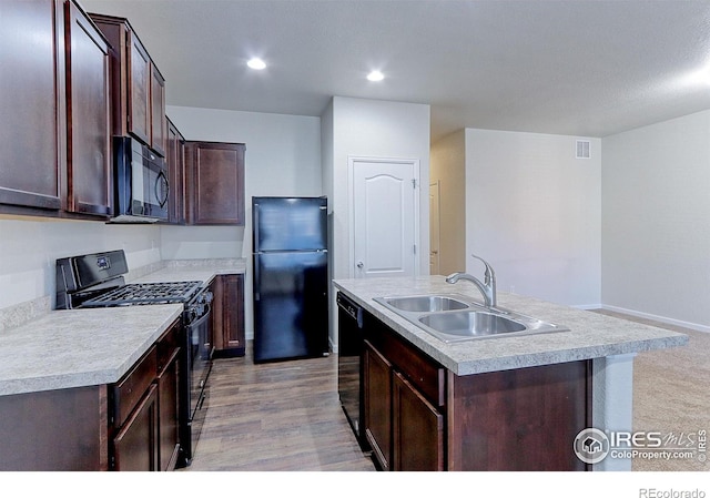 kitchen featuring black appliances, a center island with sink, sink, dark brown cabinets, and light hardwood / wood-style floors