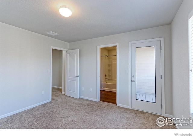 unfurnished bedroom with a textured ceiling, light carpet, and ensuite bath