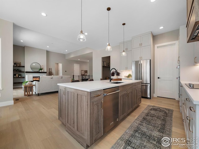 kitchen with a kitchen island with sink, a sink, a lit fireplace, stainless steel appliances, and light wood-style floors