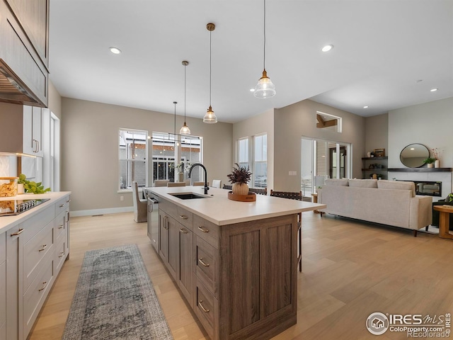 kitchen with hanging light fixtures, sink, light hardwood / wood-style floors, and a center island with sink