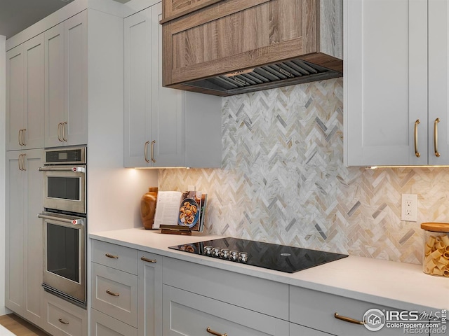 kitchen featuring custom exhaust hood, white cabinetry, black electric stovetop, double oven, and decorative backsplash