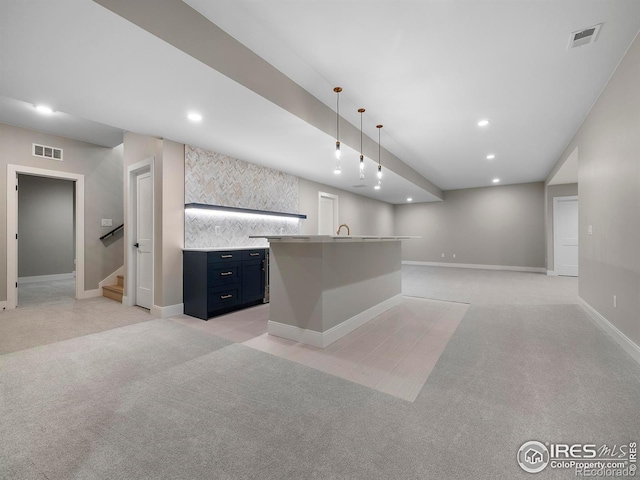 kitchen featuring decorative light fixtures, light colored carpet, a kitchen island with sink, and sink