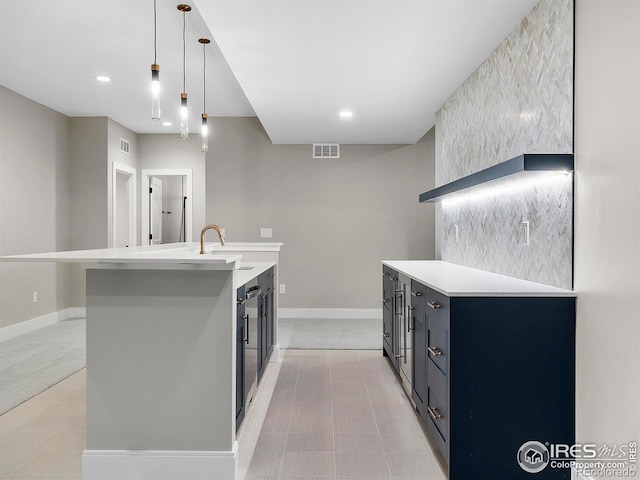 kitchen featuring decorative light fixtures, light colored carpet, a kitchen island with sink, and sink