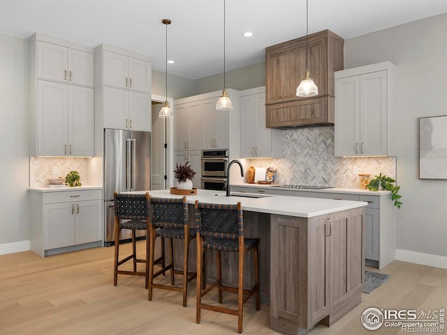 kitchen with light wood-style flooring, a sink, appliances with stainless steel finishes, a breakfast bar area, and light countertops