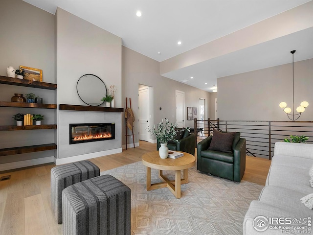 living area featuring a glass covered fireplace, a chandelier, light wood-style flooring, and recessed lighting