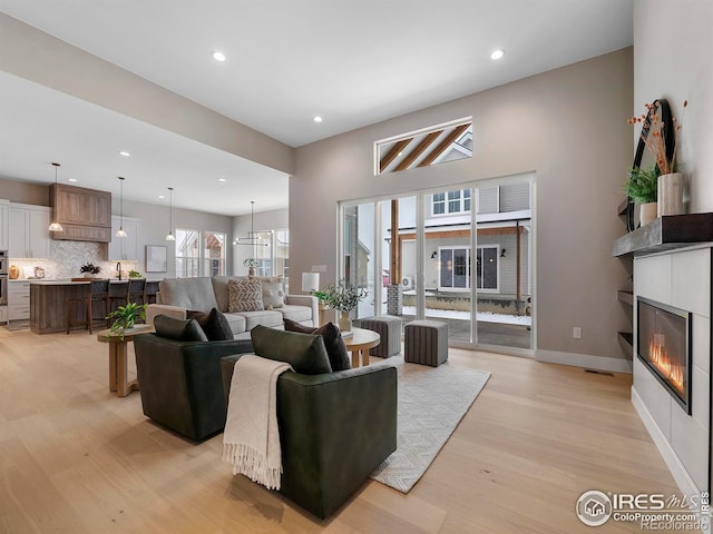 living room with recessed lighting, light wood-style flooring, baseboards, and a glass covered fireplace