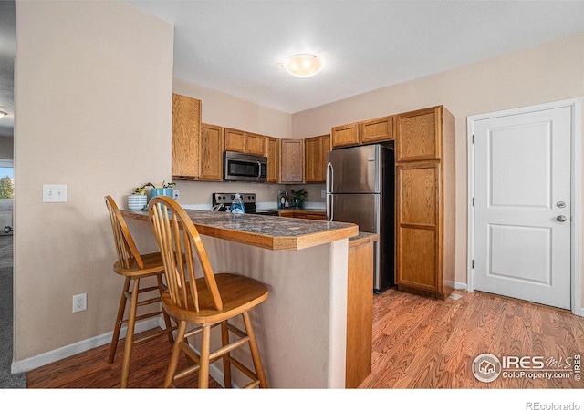 kitchen featuring a kitchen bar, kitchen peninsula, stainless steel appliances, and light wood-type flooring