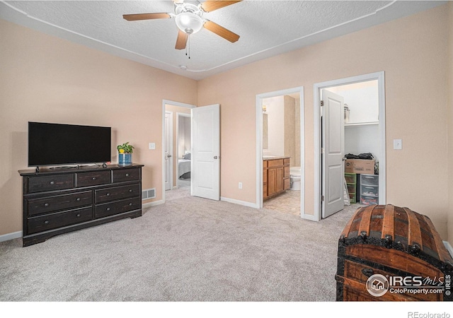 carpeted bedroom featuring ceiling fan, a walk in closet, a textured ceiling, and connected bathroom