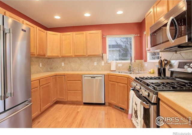 kitchen with sink, light brown cabinets, stainless steel appliances, backsplash, and light hardwood / wood-style floors