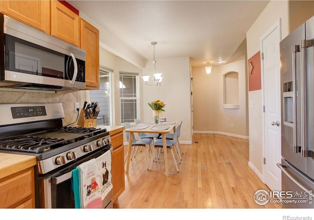 kitchen featuring decorative backsplash, light wood-type flooring, decorative light fixtures, stainless steel appliances, and a chandelier