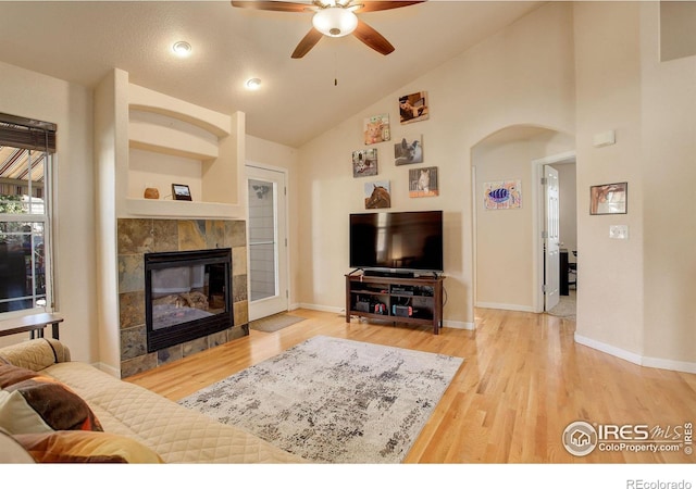 living room with hardwood / wood-style floors, ceiling fan, high vaulted ceiling, and a tiled fireplace