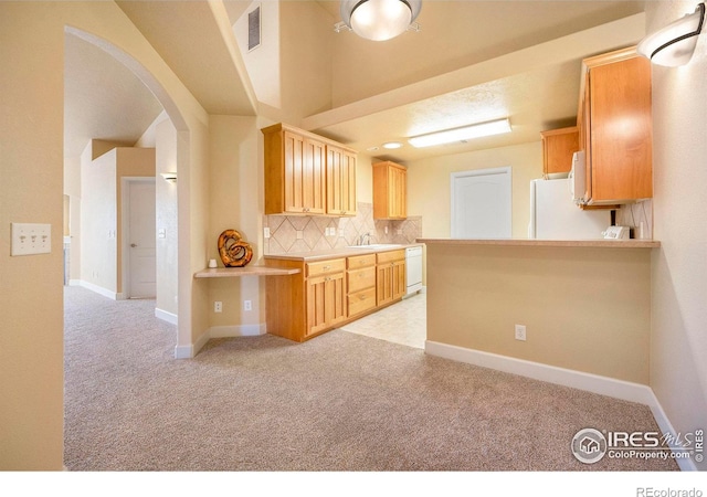 kitchen featuring white appliances, kitchen peninsula, light carpet, and light brown cabinetry