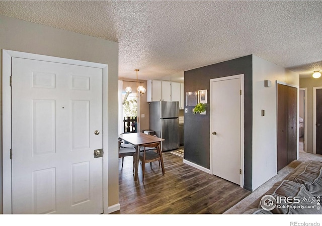 kitchen featuring stainless steel refrigerator, dark wood-type flooring, a notable chandelier, a textured ceiling, and white cabinets