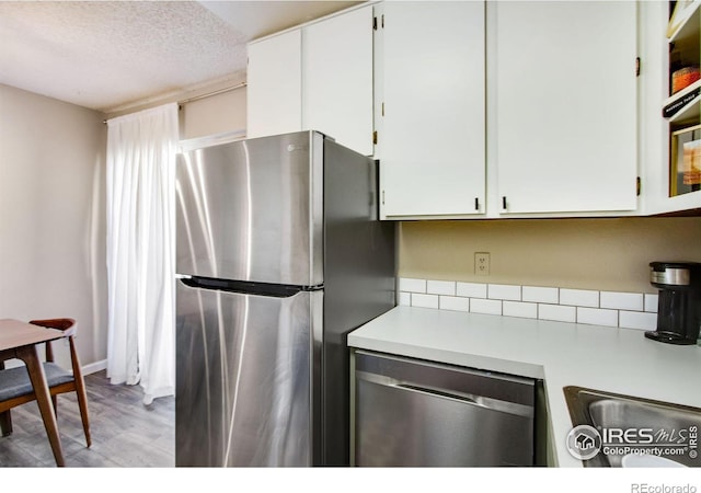 kitchen with a textured ceiling, light wood-style flooring, white cabinets, light countertops, and appliances with stainless steel finishes