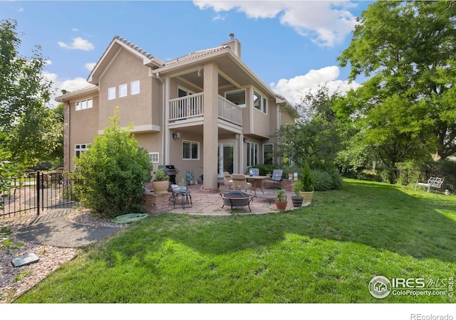 back of house featuring a lawn, a balcony, a patio, and a fire pit