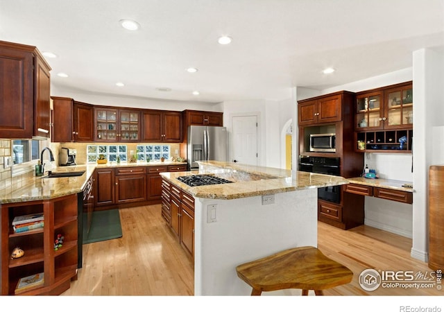 kitchen featuring light stone countertops, sink, a center island, light hardwood / wood-style flooring, and appliances with stainless steel finishes