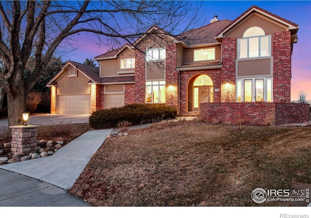 traditional home featuring a garage, a tiled roof, concrete driveway, stucco siding, and a chimney