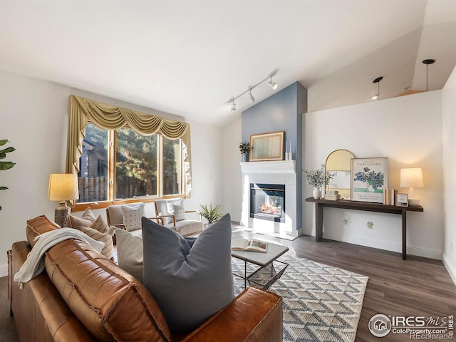 living room featuring a tile fireplace, dark hardwood / wood-style flooring, track lighting, and lofted ceiling