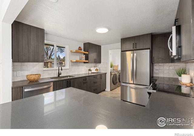 kitchen featuring washing machine and clothes dryer, sink, dark brown cabinets, and appliances with stainless steel finishes