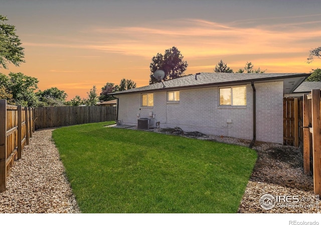 back house at dusk featuring a yard and central AC