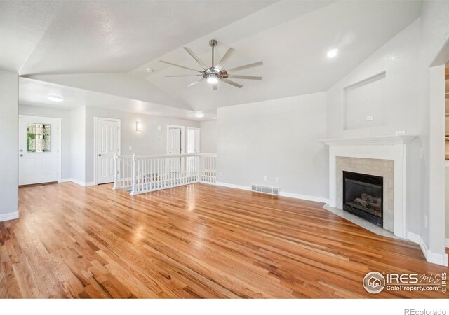 unfurnished living room with ceiling fan, light wood-type flooring, a tile fireplace, and vaulted ceiling