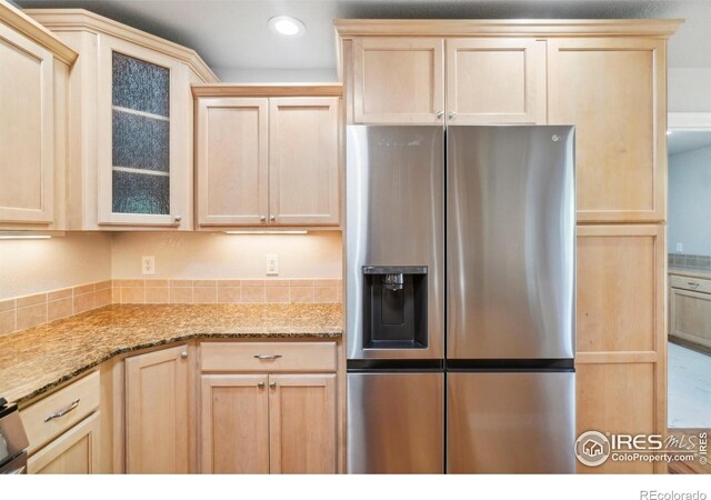 kitchen with stainless steel fridge, light stone counters, and light brown cabinets